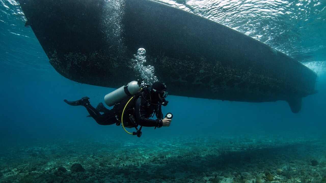 Scuba diver underwater beneath a boat hull